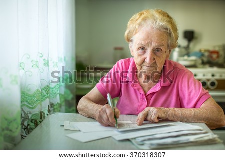 An elderly woman fills in utility bills.