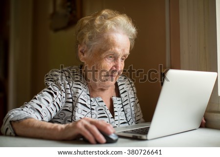 Elderly woman working on laptop sitting near the window.