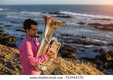 Young musician playing the trumpet on the ocean coast.