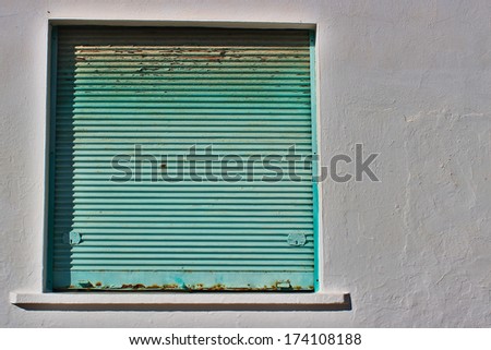 Green rusty metal window shutter on stucco wall