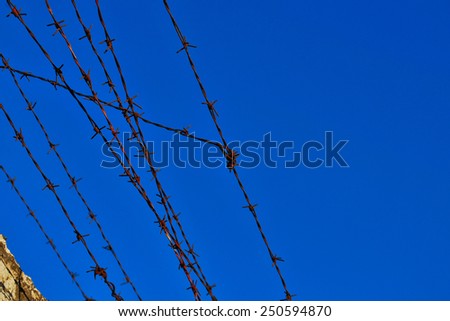Old rusty barbed wire fence atop concrete wall