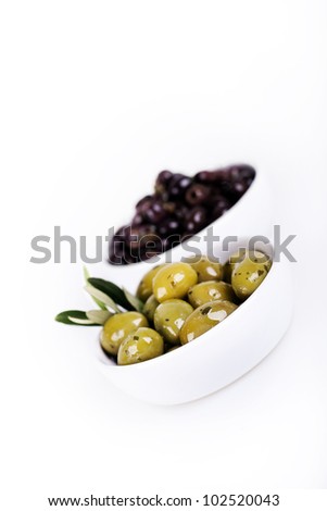 Green and black olives in white bowls over white. Intentional shallow depth of field.