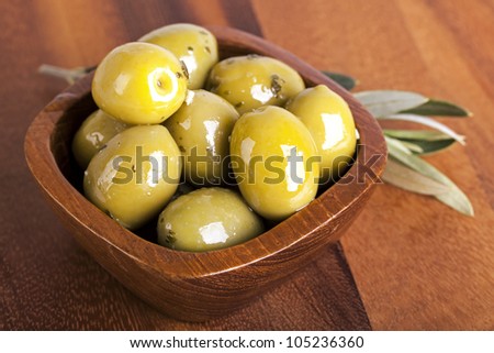 Green olives in a wooden bowl with olive branch, on wooden background.