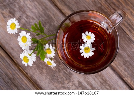 Glass cup of camomile tea with camomile flowers, on vintage wood table.