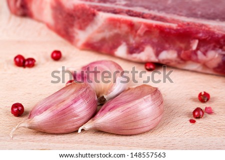 Closeup of cloves of garlic and pink peppercorns with a beef steak in the background, on wooden surface. Intentional shallow depth of field.