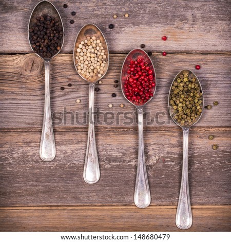 Tarnished silver spoons containing black, white, pink and green peppercorns over old wood background. Vintage style processing.
