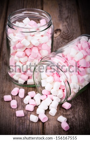 Pink and white marshmallows spilling from a storage jar, over old wood background. Vintage effect with intentional vignette
