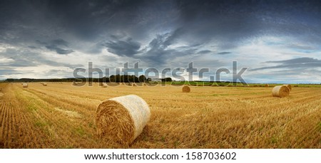 Panorama of straw bales in a field under a dramatic, stormy sky. Rural Scotland between Elgin and Lossiemouth.