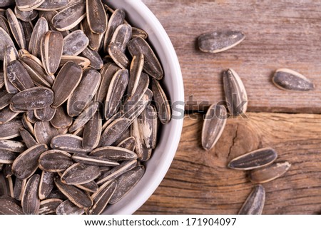 Roasted and salted sunflowers seeds in their shells, in white ceramic bowl over old wood background.