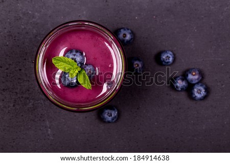 Blueberry smoothie in a glass jar with fresh berries and mint garnish, on a chalk board background