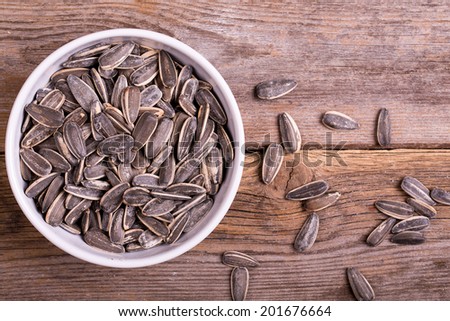 Sunflower seeds in a white ceramic bowl, over old wood background
