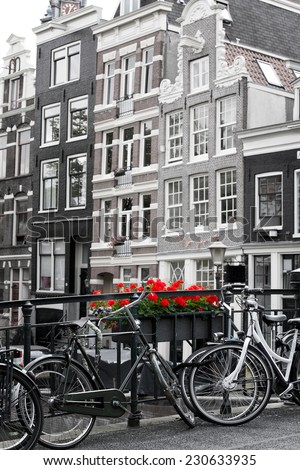 Amsterdam street scene with old bicycles against a backdrop of traditional Merchant houses. Black and white with selective colouring on flowers.
