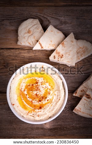 A bowl of fresh hummus, drizzled with olive oil and paprika, served with wedges of pita bread.