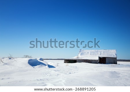 Old wooden barn in Quebec province of Canada. Rural snow scene with snow drifts and blue sky. SPace for your text.
