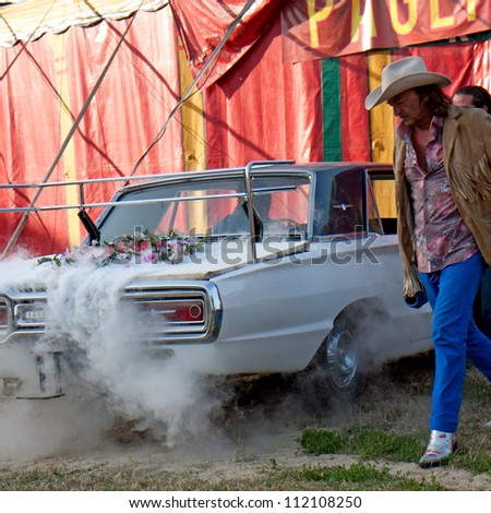 AURILLAC, FRANCE - AUGUST 22: some smoke comes from the engine of a vintage car near a big top, Aurillac International Street Theater Festival, Company Off ,on august 22, 2012, in Aurillac,France.