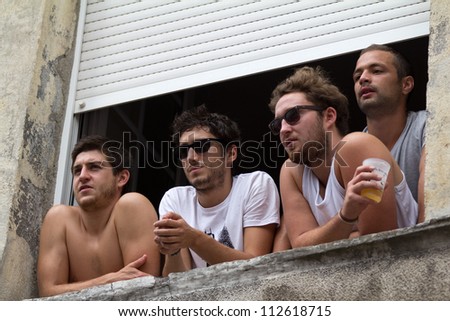 AURILLAC, FRANCE - AUGUST 22: four young men look at a show from a window during the Aurillac International Street Theater Festival, on august 22, 2012, in Aurillac,France.