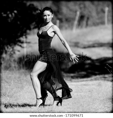 Young woman wearing a black dress is dancing the flamenco in a country lane, France.
