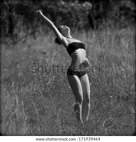Zen woman , wearing black underwear, dances at the first rays of sunlight in a field.