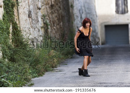 Contemporay dancer alone in a street of a french village. She wears a low-neck dress and clodhoppers.