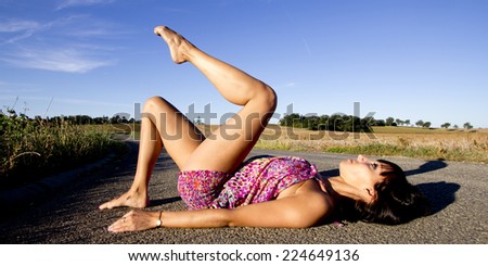 Young supple dancer lying on the back on a french country road. She raises gracefully her leg.