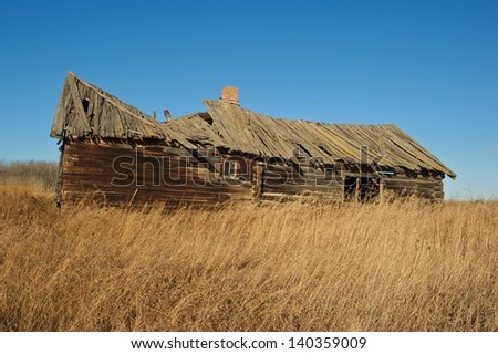 old abandoned log house in dry dead grass in fall
