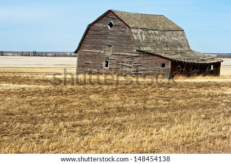 An old barn falling into ruin in a harvested field in spring