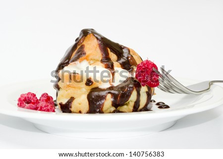 A delicious and exquisite dessert on a plate with a fork - eclair in milk chocolate with cream and fresh raspberries