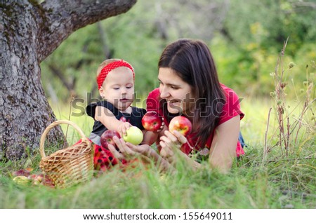 mom and her little daughter picking apples in the garden