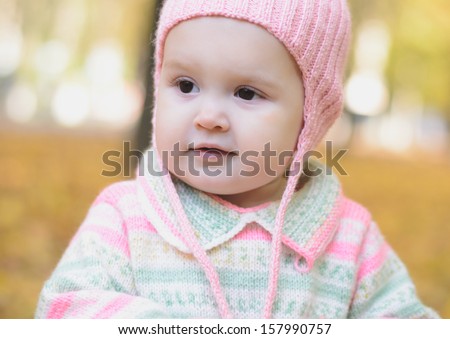 baby girl in a pink cap walks in autumn park