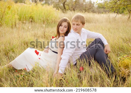 pregnant woman and her husband sitting back to back on grass and lovingly looking at each other