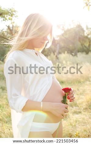 portrait of a pregnant woman in profile with red rose in her hand
