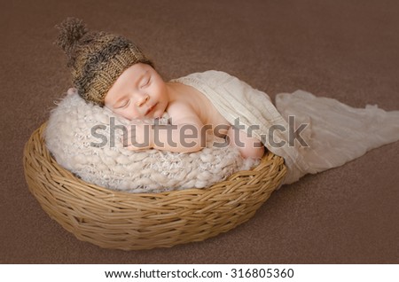 plump sweet baby sleeping on his tummy in a basket in brown knitted cap