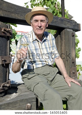 Senior man sitting on the press is tasting the white wine.