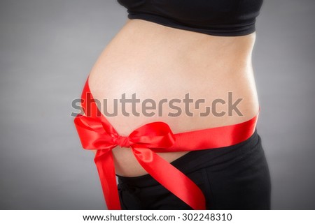 Closed-up of pregnant woman without hand over tummy at gray background.