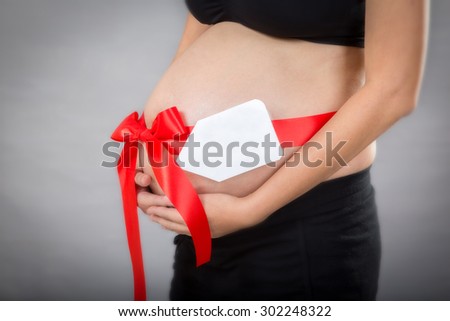 Closed-up of pregnant woman with name tag and on hand over tummy at gray background.