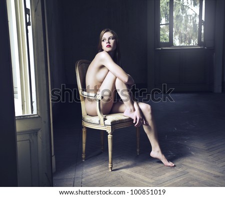Beautiful naked woman sitting on an old chair in an empty room