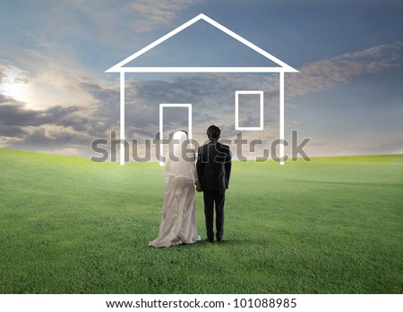 Married couple walking on a green meadow towards the shape of a house