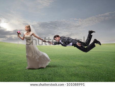 Impatient happy wife pulling her husband by his arm and running on a green meadow
