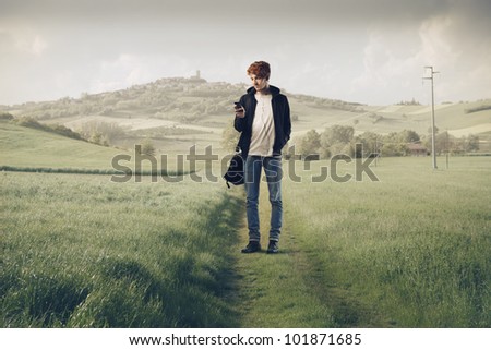 Young man on a country pathway carrying a rucksack and using a mobile phone