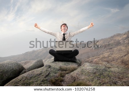 Young businessman sitting on a rock and triumphing with a laptop on his knees
