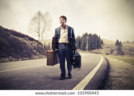 Young man tired of walking and carrying suitcases on a country road
