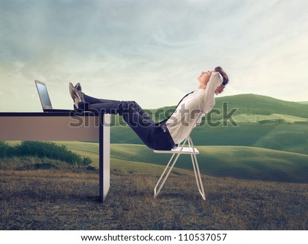 Young businessman relaxing at his desk in the middle of a green meadow
