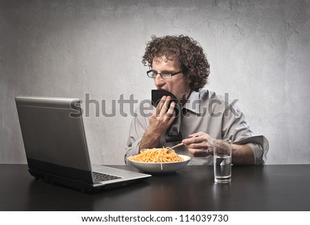 Man eating pasta while using a laptop computer