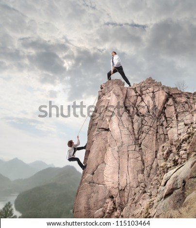 Businessman on the top of a rock helping an other businessman to climb it