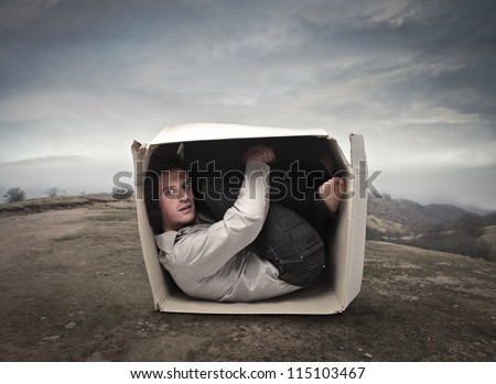 Man crouched into a box in a wasteland
