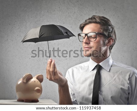 Businessman protecting a piggy with a little black umbrella - stock photo