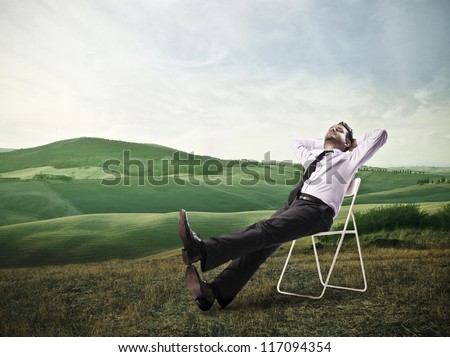 Office worker is lying on a chair in a large grace field
