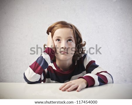 A bored red child is thinking while is leaning on a white desk