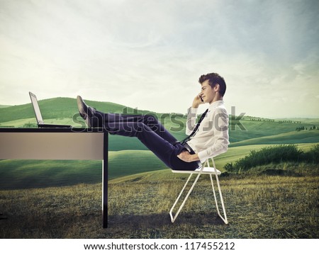 Young businessman calling. in a large grace field, with his feet on his desk