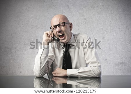 A bald office worker screams while is calling someone with a mobile phone